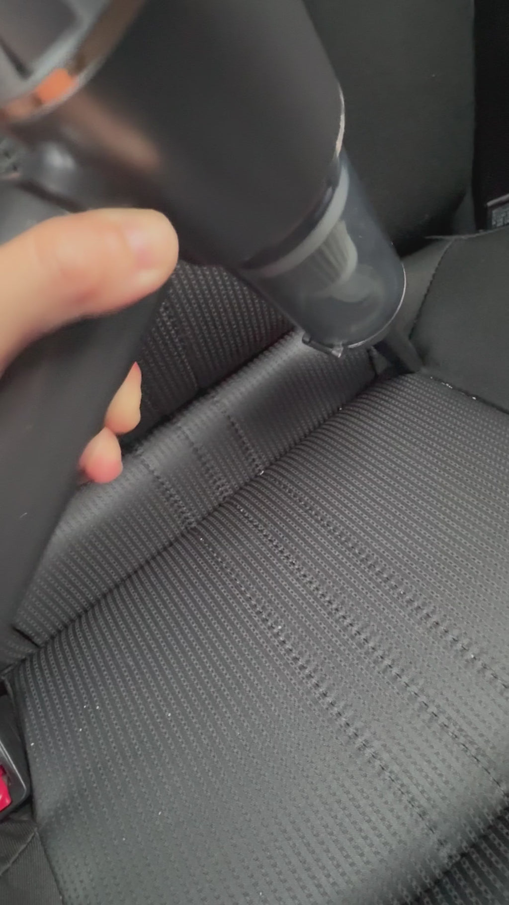 A handheld cordless vacuum cleaning crumbs from a car seat, demonstrating its strong suction and portability.